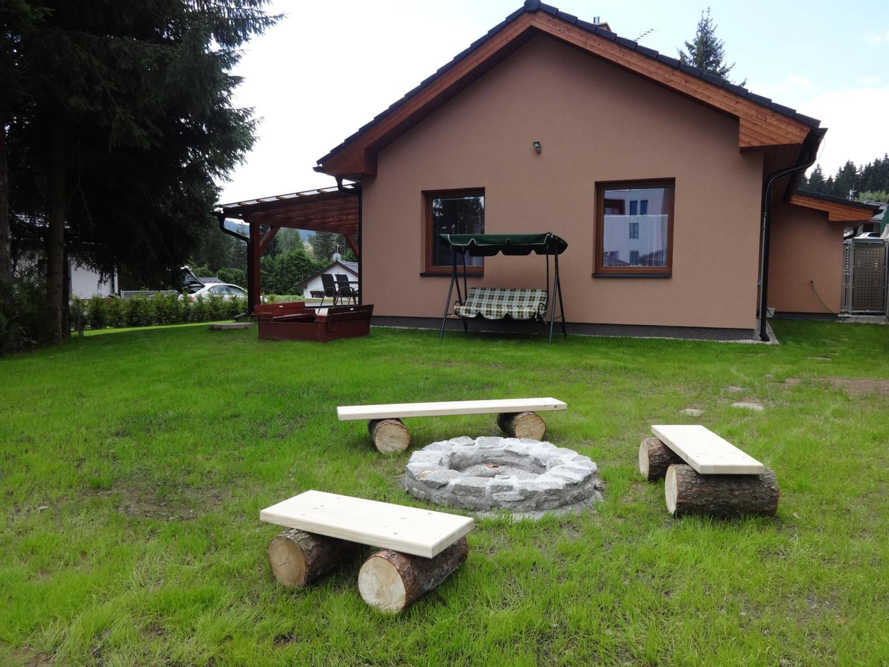 Zahrada chaty s ohništěm a dřevěnými lavičkami
